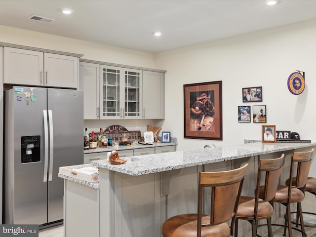 kitchen with a kitchen bar, light stone countertops, stainless steel refrigerator with ice dispenser, and gray cabinetry