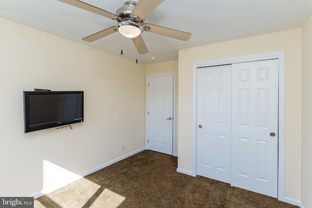 unfurnished bedroom with ceiling fan, dark colored carpet, and a closet