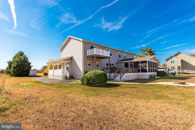 rear view of house with a balcony, a lawn, a patio, and a sunroom