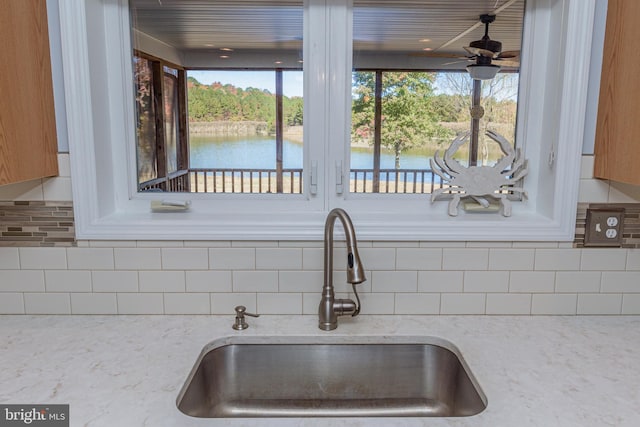 kitchen with light stone counters, sink, a water view, and decorative backsplash