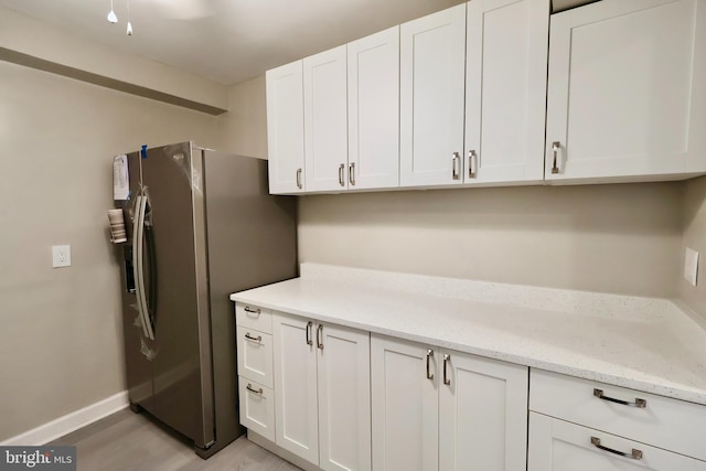 kitchen with white cabinets, light wood-type flooring, light stone countertops, and stainless steel fridge with ice dispenser