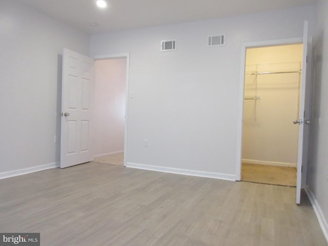 unfurnished bedroom featuring a closet, a spacious closet, and light hardwood / wood-style flooring