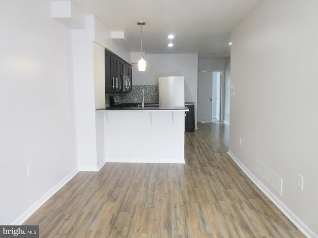 kitchen with refrigerator, hardwood / wood-style floors, tasteful backsplash, decorative light fixtures, and kitchen peninsula