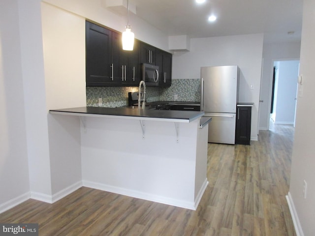 kitchen featuring a kitchen breakfast bar, kitchen peninsula, pendant lighting, stainless steel appliances, and decorative backsplash