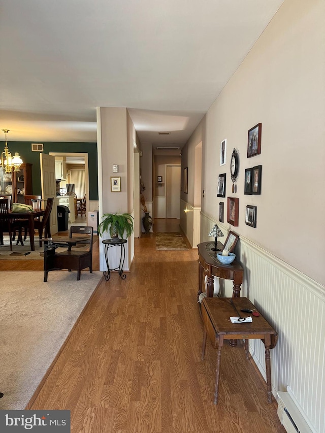 hall featuring hardwood / wood-style flooring, a chandelier, and baseboard heating