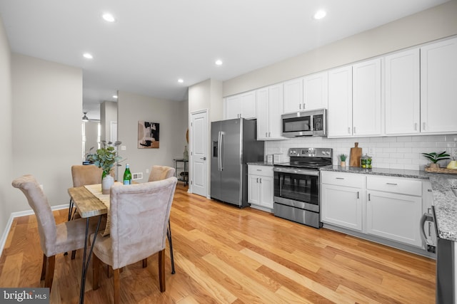 kitchen featuring white cabinetry, stainless steel appliances, light stone counters, backsplash, and light hardwood / wood-style floors