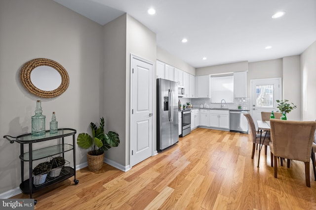 kitchen featuring sink, stainless steel appliances, backsplash, light hardwood / wood-style floors, and white cabinets