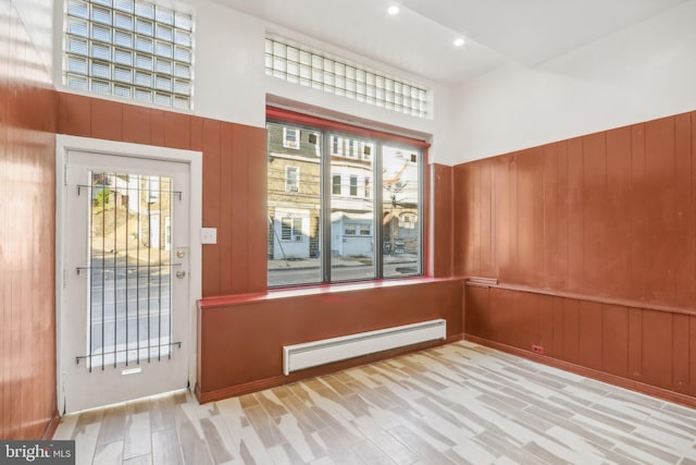 empty room featuring baseboard heating, wooden walls, a towering ceiling, and light hardwood / wood-style floors