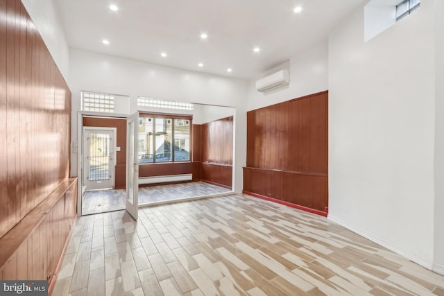 entrance foyer with a towering ceiling, light hardwood / wood-style flooring, a wall mounted air conditioner, and wooden walls