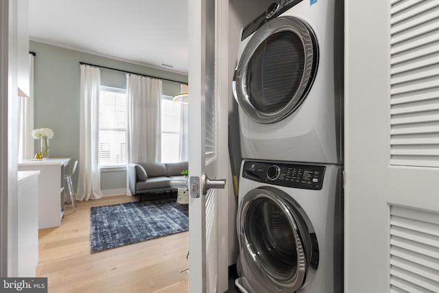 clothes washing area with light hardwood / wood-style flooring and stacked washing maching and dryer