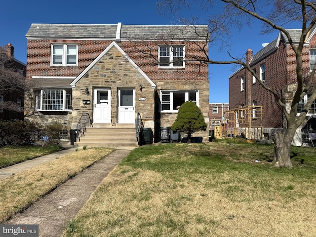 english style home featuring a front yard, stone siding, and brick siding