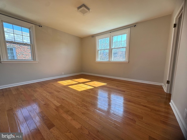 empty room with a healthy amount of sunlight, hardwood / wood-style flooring, visible vents, and baseboards