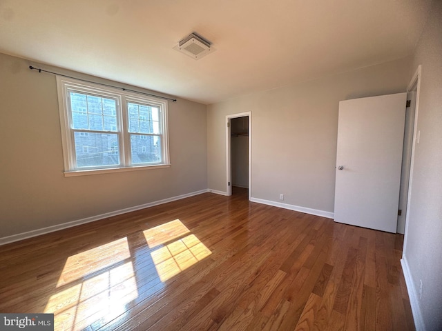 unfurnished bedroom with baseboards, visible vents, wood finished floors, and a walk in closet