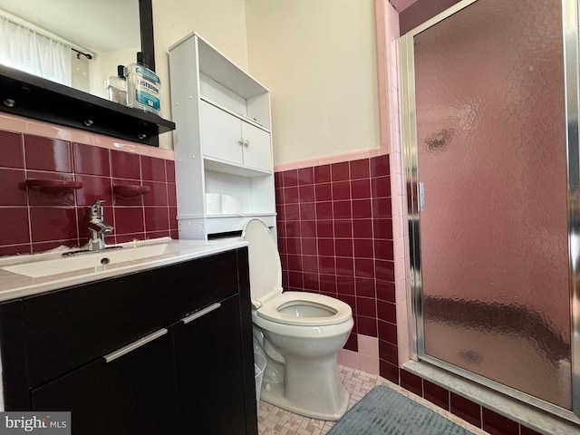 bathroom featuring a shower with door, toilet, tile walls, vanity, and tile patterned flooring