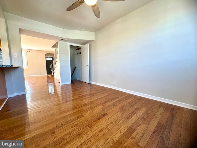 unfurnished room featuring arched walkways, a ceiling fan, wood finished floors, and baseboards
