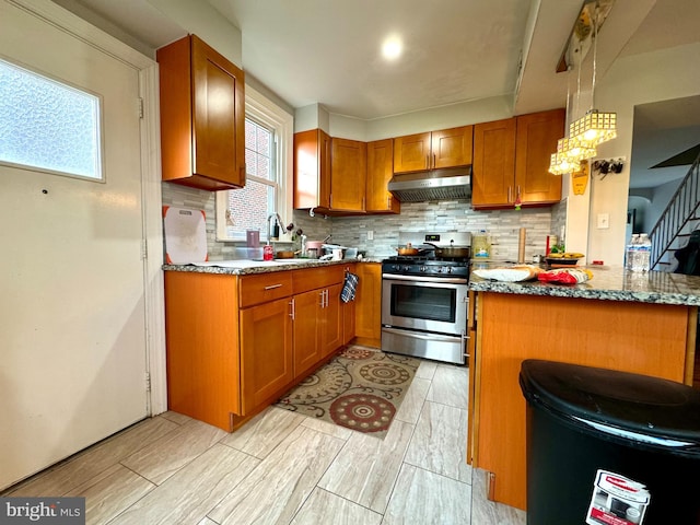 kitchen with tasteful backsplash, light stone countertops, kitchen peninsula, hanging light fixtures, and stainless steel stove