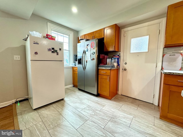 kitchen featuring stainless steel refrigerator with ice dispenser, decorative backsplash, and white fridge