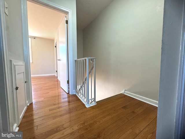 hall featuring baseboards, wood finished floors, and an upstairs landing