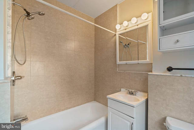 full bathroom featuring tiled shower / bath, vanity, toilet, and tile walls