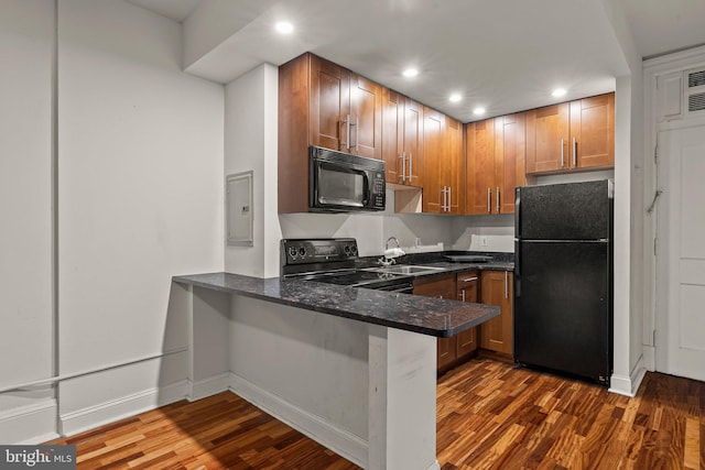 kitchen with kitchen peninsula, dark hardwood / wood-style floors, dark stone countertops, black appliances, and sink