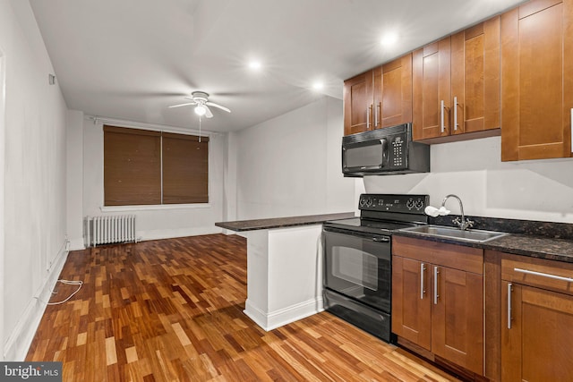 kitchen with hardwood / wood-style floors, sink, black appliances, and radiator