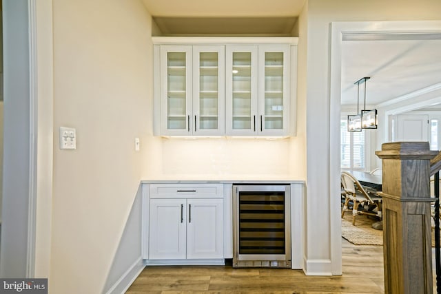 bar featuring hanging light fixtures, wine cooler, crown molding, light wood-type flooring, and white cabinets