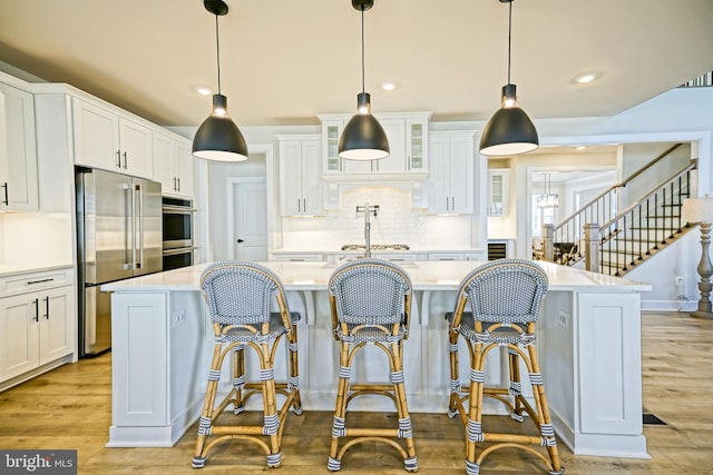 kitchen featuring white cabinetry, a kitchen island with sink, pendant lighting, light hardwood / wood-style floors, and stainless steel appliances