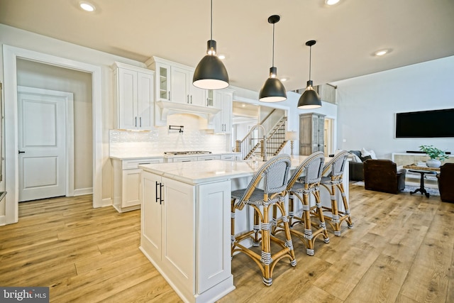 kitchen with white cabinets, pendant lighting, light wood-type flooring, and an island with sink