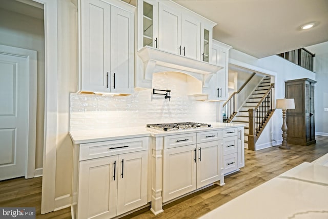 kitchen with stainless steel gas cooktop, white cabinetry, hardwood / wood-style floors, and backsplash