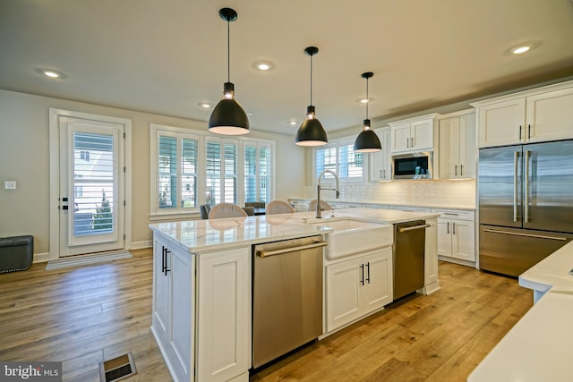 kitchen with a sink, stainless steel appliances, a center island with sink, backsplash, and white cabinetry