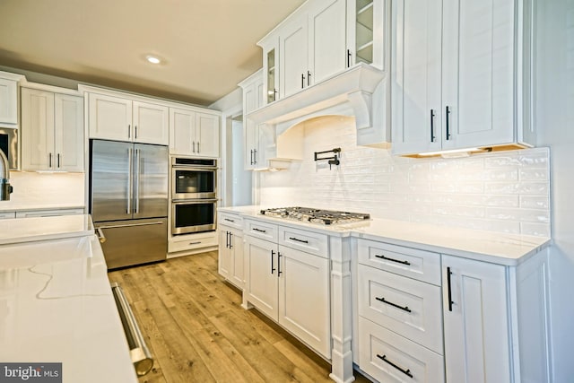 kitchen featuring white cabinets, backsplash, appliances with stainless steel finishes, light stone countertops, and light hardwood / wood-style flooring