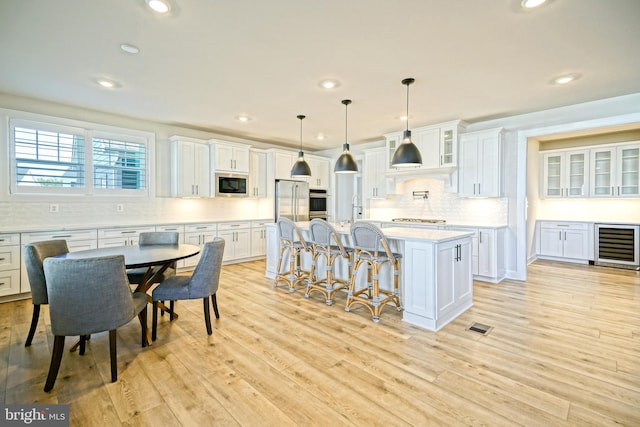 kitchen with a kitchen island, white cabinetry, stainless steel appliances, decorative light fixtures, and light hardwood / wood-style flooring