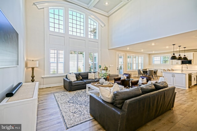 living room with a high ceiling, recessed lighting, ornamental molding, and light wood-style floors
