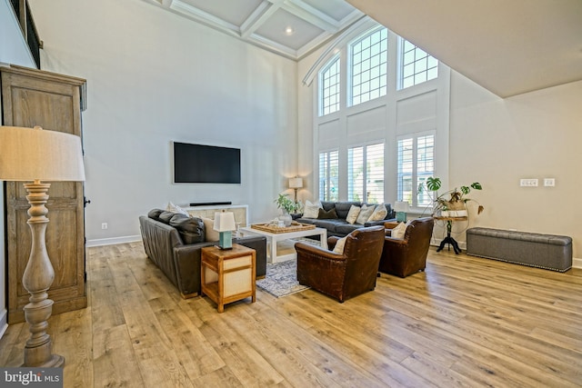 living room featuring coffered ceiling, beamed ceiling, light wood finished floors, baseboards, and a towering ceiling