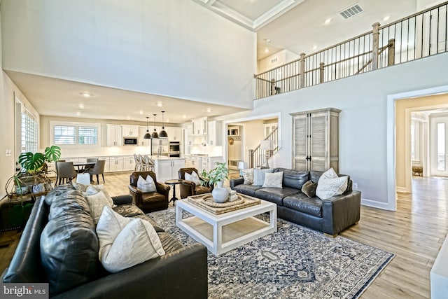 living room with light wood-style floors, visible vents, stairs, and a towering ceiling