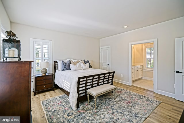 bedroom with connected bathroom, light wood-style flooring, and baseboards