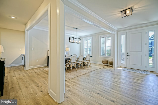 foyer featuring crown molding, a notable chandelier, light wood-style flooring, and plenty of natural light