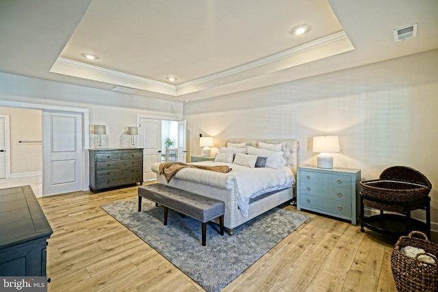 bedroom with visible vents, light wood-style flooring, ornamental molding, and a tray ceiling