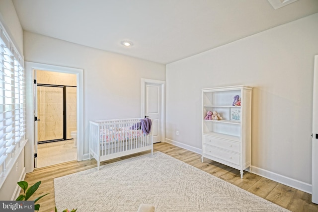 unfurnished bedroom featuring connected bathroom, hardwood / wood-style flooring, and a crib