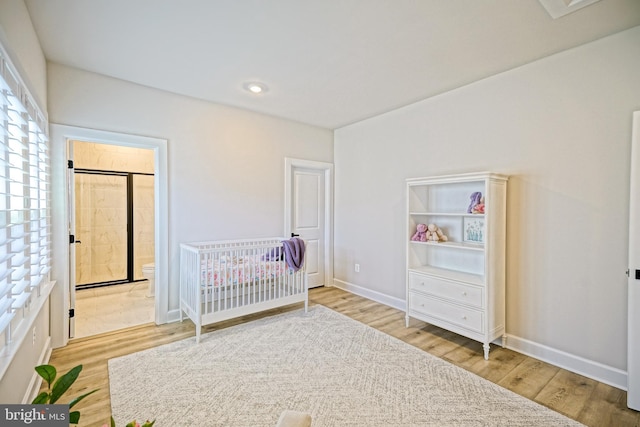 bedroom with recessed lighting, wood finished floors, a crib, ensuite bathroom, and baseboards