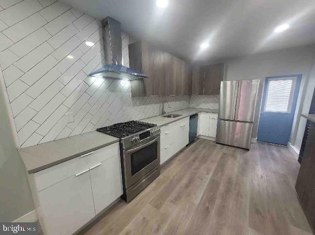 kitchen with wall chimney range hood, white cabinetry, sink, light hardwood / wood-style floors, and stainless steel appliances