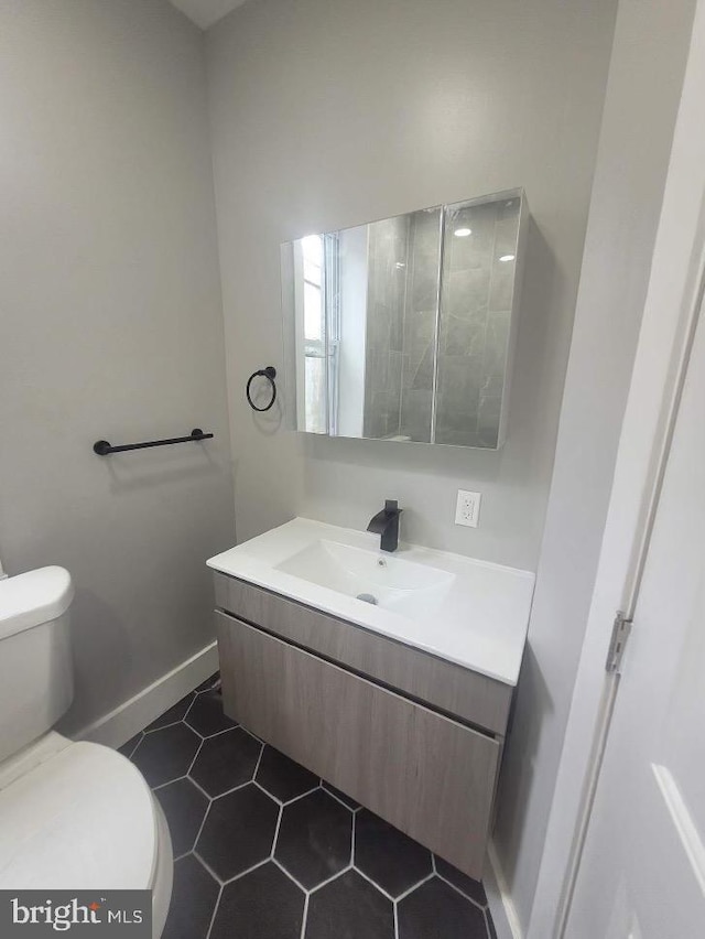 half bathroom featuring toilet, tile patterned flooring, vanity, and baseboards