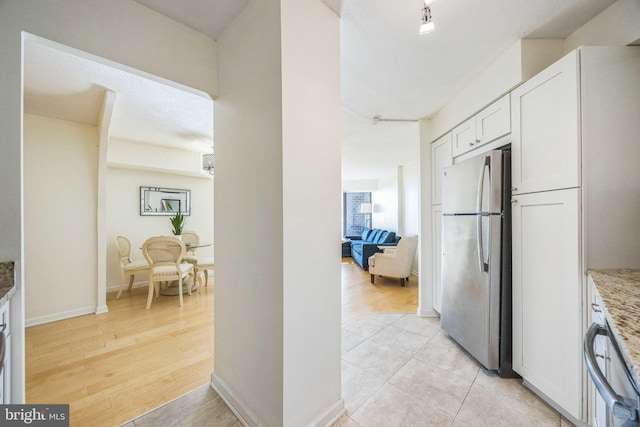 kitchen featuring light hardwood / wood-style flooring, light stone counters, white cabinets, and stainless steel refrigerator