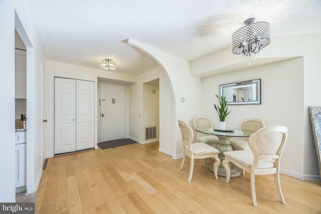 dining area with light hardwood / wood-style flooring, a textured ceiling, and a notable chandelier