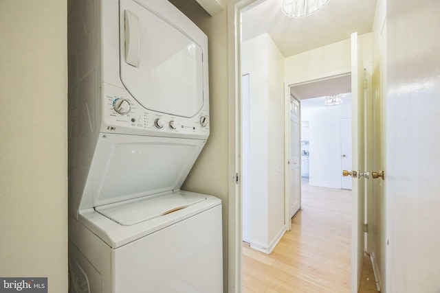 laundry area featuring stacked washing maching and dryer and light hardwood / wood-style flooring