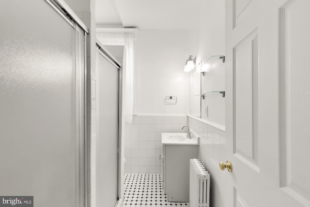 bathroom with radiator, tile walls, a shower with shower door, and vanity