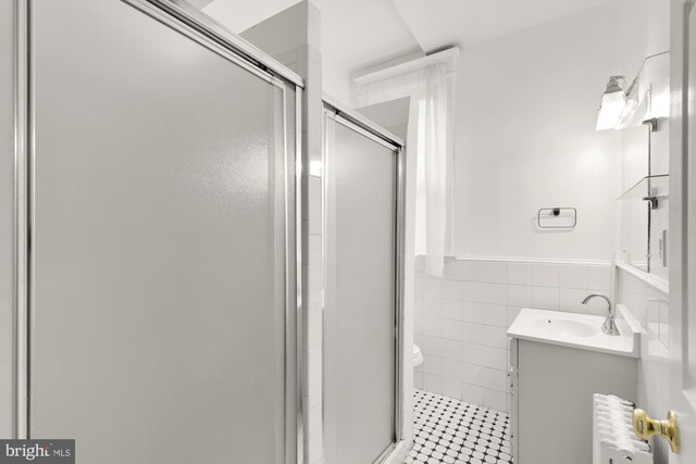 bathroom featuring a shower with door, radiator, toilet, tile walls, and vanity