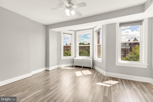 empty room with light hardwood / wood-style flooring, radiator heating unit, and a healthy amount of sunlight