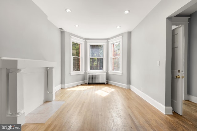 unfurnished living room featuring decorative columns, light hardwood / wood-style flooring, and radiator heating unit