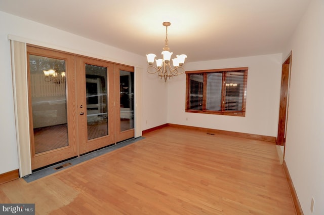 unfurnished dining area featuring french doors, wood-type flooring, and a chandelier